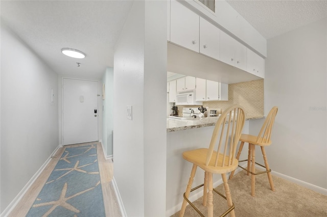 1501 Beach Rd Unit 310, Englewood, FL 34223 - kitchen featuring white microwave, a kitchen bar, range, white cabinets, and baseboards