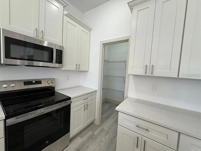 311 Yule St, Port Charlotte, FL 33953 - kitchen featuring appliances with stainless steel finishes, light wood-style floors, light stone countertops, and white cabinets