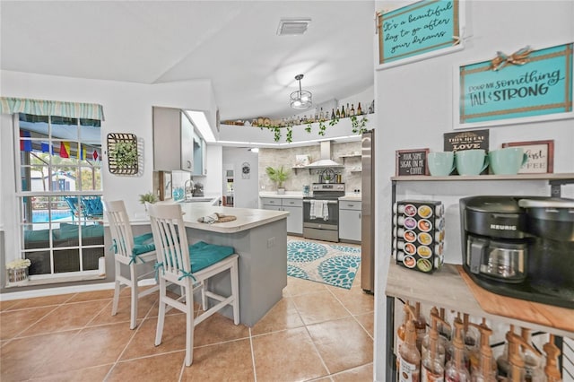 13703 Drysdale Ave, Port Charlotte, FL 33981 - kitchen with stainless steel appliances, wall chimney range hood, light tile patterned floors, light countertops, and lofted ceiling