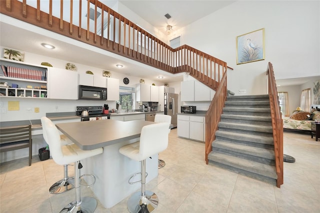 196 Lecturn St, Port Charlotte, FL 33954 - kitchen featuring black appliances, a towering ceiling, white cabinets, light tile patterned flooring, and a kitchen breakfast bar