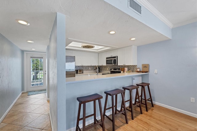 7554 Palm Island Dr S Unit 1813, Placida, FL 33946 - kitchen featuring appliances with stainless steel finishes, white cabinetry, decorative backsplash, crown molding, and a kitchen breakfast bar