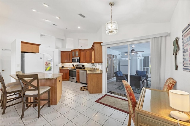 727 Rotonda Cir, Rotonda West, FL 33947 - kitchen featuring stainless steel appliances, brown cabinetry, a breakfast bar, light stone countertops, and vaulted ceiling