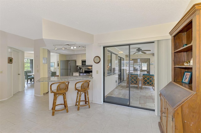 7218 Darlington St, Englewood, FL 34224 - kitchen with stainless steel appliances, a ceiling fan, a textured ceiling, a breakfast bar area, and a peninsula