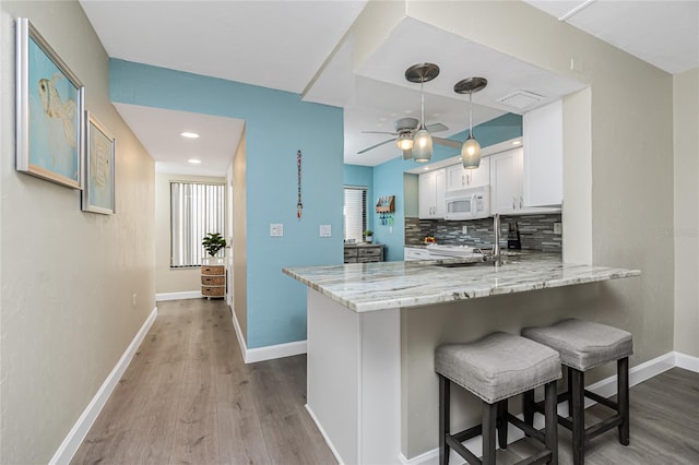 2955 N Beach Rd Unit A411, Englewood, FL 34223 - kitchen featuring white microwave, white cabinets, wood finished floors, a peninsula, and light stone countertops