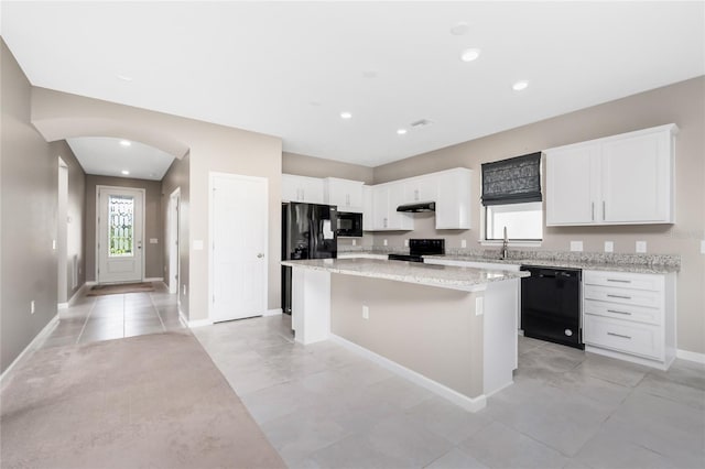 1530 Hyssop Loop, North Port, FL 34289 - kitchen featuring black appliances, a kitchen island, under cabinet range hood, white cabinetry, and light stone countertops