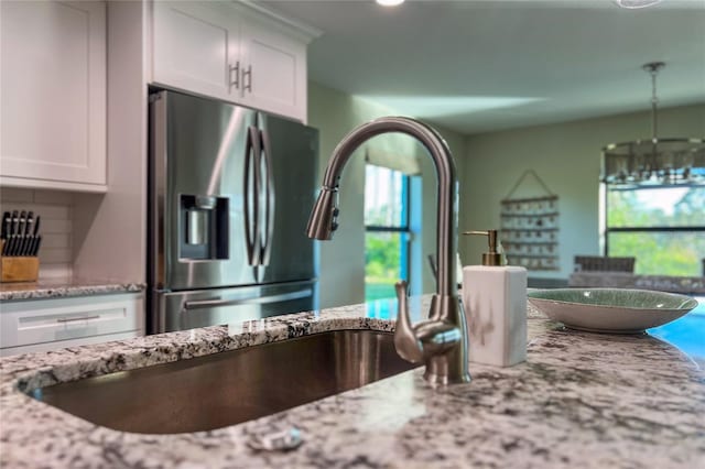 184 Spring Dr, Rotonda West, FL 33947 - kitchen with stainless steel fridge with ice dispenser, light stone counters, white cabinets, recessed lighting, and a chandelier