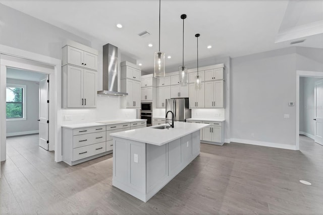 14089 Wenzel Ave, Port Charlotte, FL 33981 - kitchen featuring wall chimney range hood, stainless steel appliances, a kitchen island with sink, light wood-style floors, and light countertops