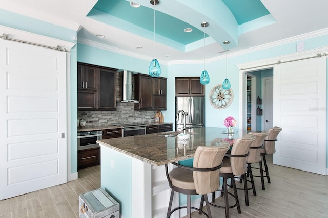 1131 Rotonda Cir, Rotonda West, FL 33947 - kitchen with a barn door, wall chimney range hood, appliances with stainless steel finishes, a raised ceiling, and ornamental molding