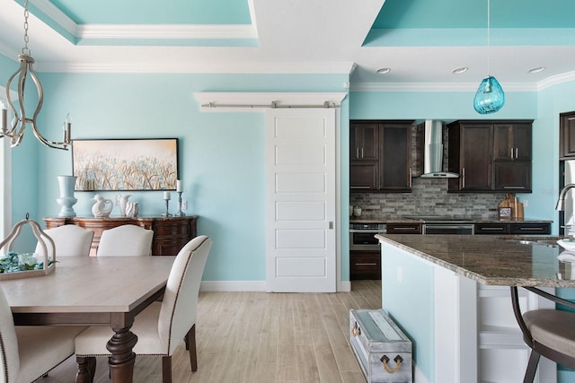 1131 Rotonda Cir, Rotonda West, FL 33947 - kitchen with wall chimney exhaust hood, a tray ceiling, dark brown cabinets, crown molding, and decorative backsplash