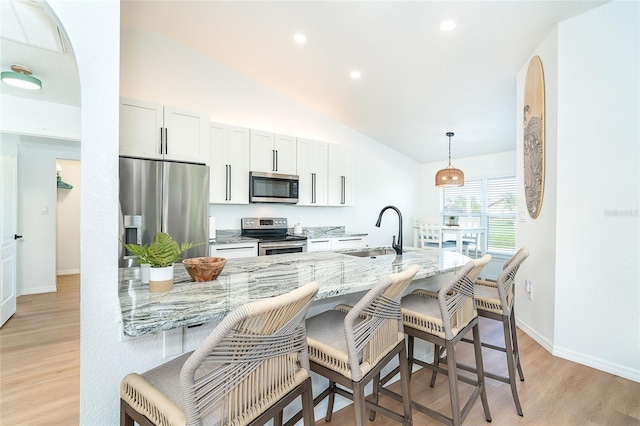 172 Mariner Ln, Rotonda West, FL 33947 - kitchen featuring stainless steel appliances, a breakfast bar area, lofted ceiling, light stone countertops, and light wood-style floors
