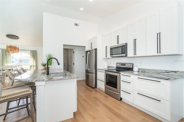 172 Mariner Ln, Rotonda West, FL 33947 - kitchen with stainless steel appliances, a kitchen breakfast bar, white cabinets, light stone counters, and light wood-type flooring