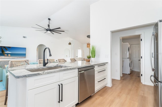 172 Mariner Ln, Rotonda West, FL 33947 - kitchen featuring appliances with stainless steel finishes, stacked washing machine and dryer, vaulted ceiling, light wood-style flooring, and white cabinets