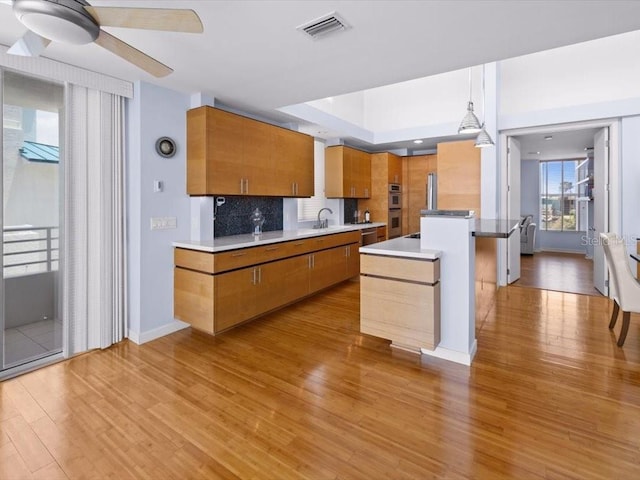 8041 Bay Pointe Dr, Englewood, FL 34224 - kitchen with light wood-type flooring, brown cabinetry, double oven, a ceiling fan, and decorative backsplash