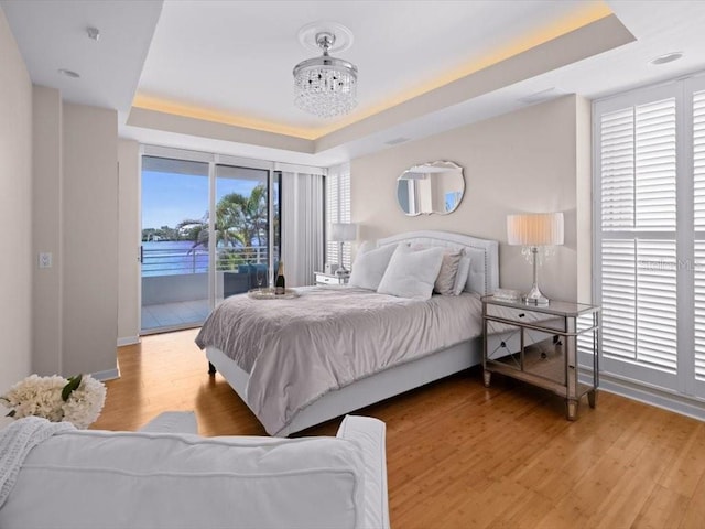 8041 Bay Pointe Dr, Englewood, FL 34224 - bedroom featuring a tray ceiling, access to exterior, wood finished floors, and a chandelier