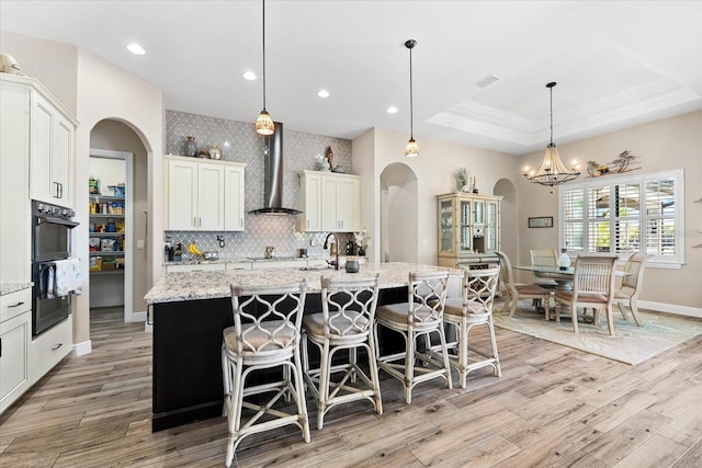 15044 San Domingo Blvd, Port Charlotte, FL 33981 - kitchen with arched walkways, wall chimney exhaust hood, black appliances, light wood-type flooring, and a kitchen bar