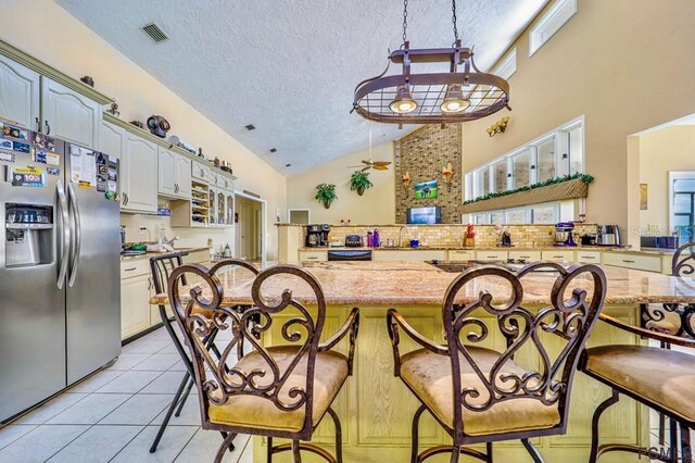 kitchen featuring high vaulted ceiling, a breakfast bar area, light tile patterned floors, stainless steel refrigerator with ice dispenser, and a textured ceiling