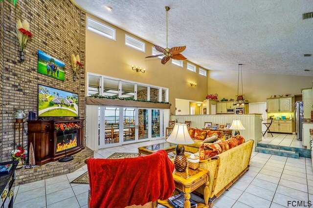 living room featuring ceiling fan, a high ceiling, a textured ceiling, light tile patterned flooring, and a brick fireplace