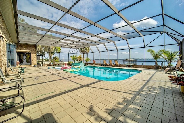 view of swimming pool featuring a patio area, a water view, and glass enclosure