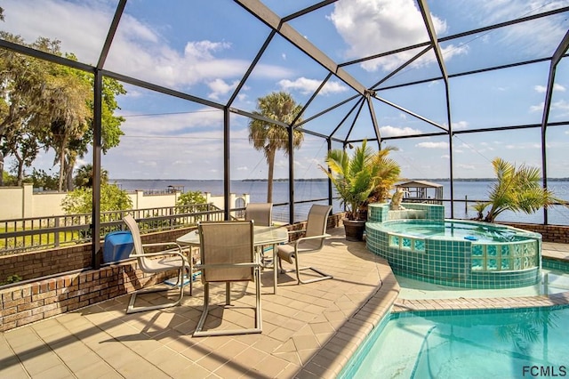 view of swimming pool with an in ground hot tub, pool water feature, glass enclosure, a water view, and a patio area