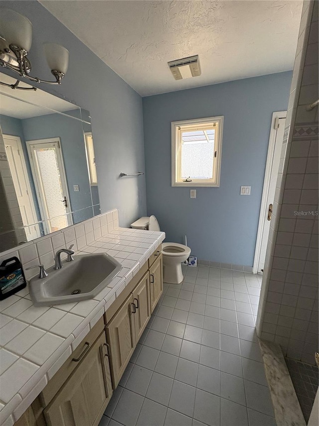 bathroom featuring tile patterned floors, toilet, a shower, a textured ceiling, and vanity