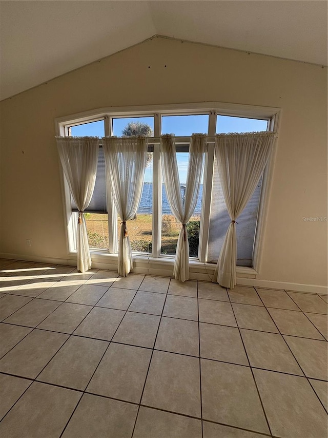 spare room with light tile patterned floors, vaulted ceiling, a healthy amount of sunlight, and a water view