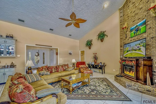 living room with light tile patterned floors, high vaulted ceiling, a brick fireplace, and ceiling fan