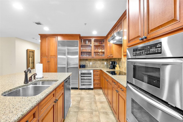 kitchen with light stone counters, appliances with stainless steel finishes, beverage cooler, and sink