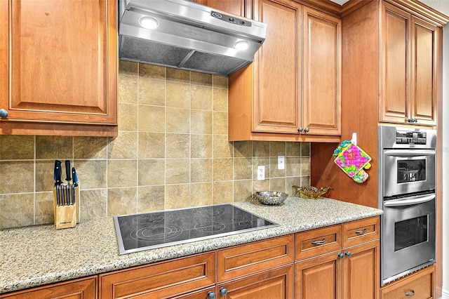 kitchen with tasteful backsplash, light stone countertops, stainless steel double oven, and black electric cooktop