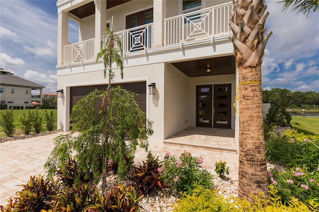 property entrance featuring decorative driveway, an attached garage, a balcony, and stucco siding