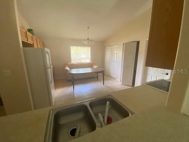 kitchen featuring pendant lighting, a notable chandelier, white fridge, light tile flooring, and vaulted ceiling