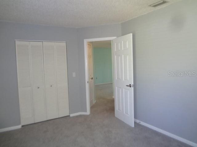 unfurnished bedroom with light carpet, a textured ceiling, and a closet