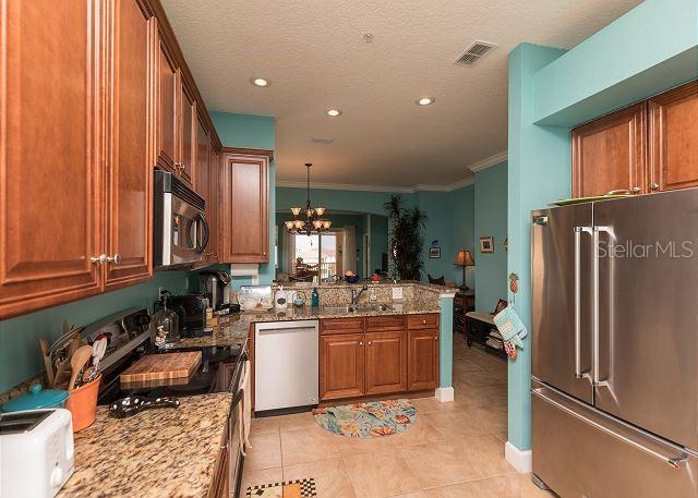 kitchen with an inviting chandelier, light stone countertops, hanging light fixtures, and stainless steel appliances