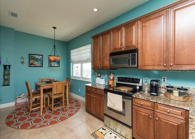 kitchen featuring light tile floors, stainless steel appliances, decorative light fixtures, and light stone counters