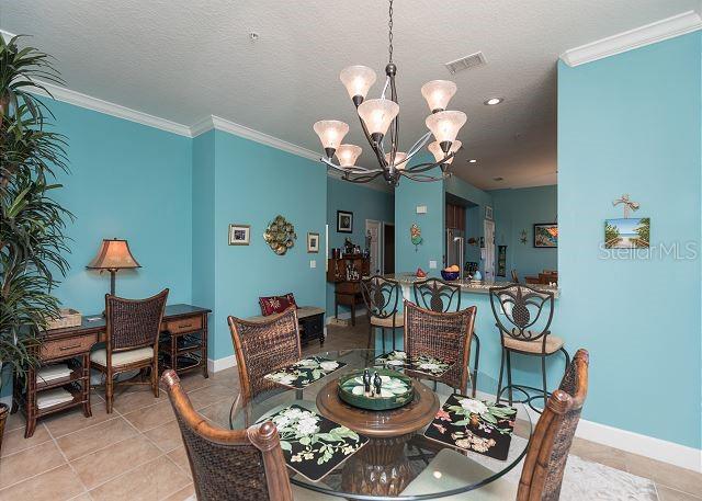 dining room with a textured ceiling, a notable chandelier, ornamental molding, and light tile floors