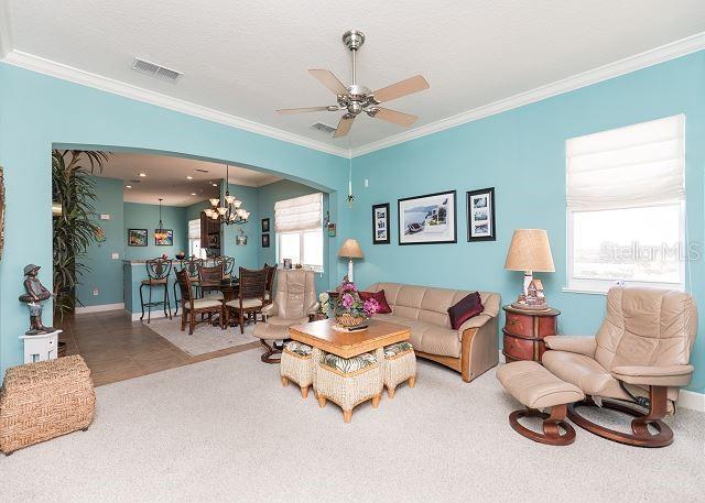 tiled living room with ornamental molding, ceiling fan with notable chandelier, and a wealth of natural light