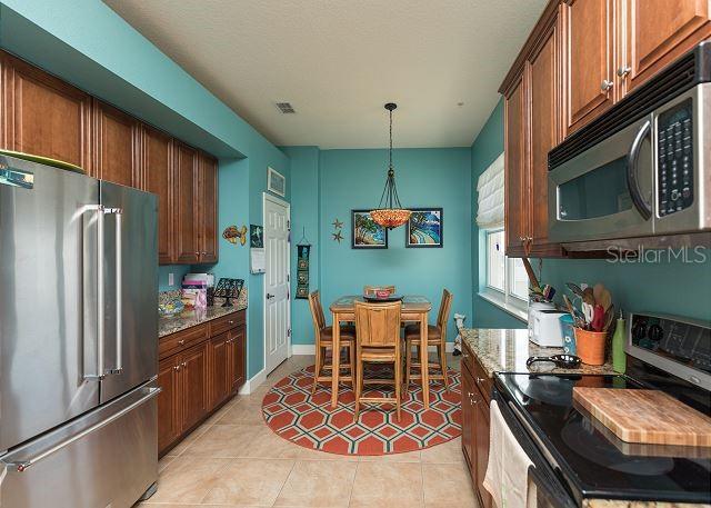 kitchen with stainless steel appliances, light tile flooring, pendant lighting, and light stone counters