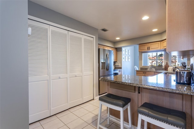 kitchen with a breakfast bar, dark stone counters, stainless steel refrigerator with ice dispenser, light tile patterned flooring, and kitchen peninsula