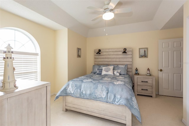 carpeted bedroom with a raised ceiling and ceiling fan