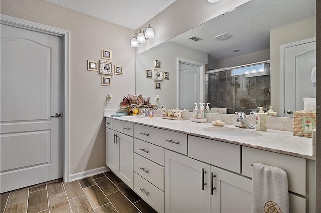 bathroom with a textured ceiling, vanity, and walk in shower