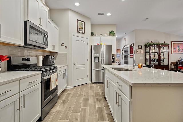 kitchen with a kitchen island with sink, white cabinets, sink, light stone counters, and stainless steel appliances