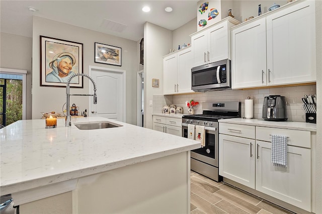 kitchen with appliances with stainless steel finishes, light stone counters, sink, white cabinetry, and an island with sink