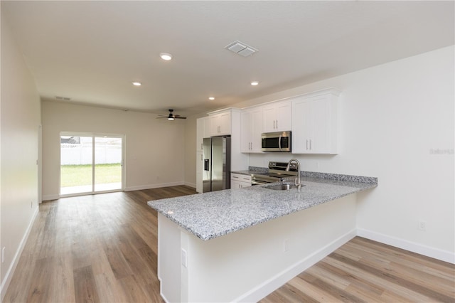 kitchen with stainless steel appliances, white cabinets, kitchen peninsula, and light stone counters