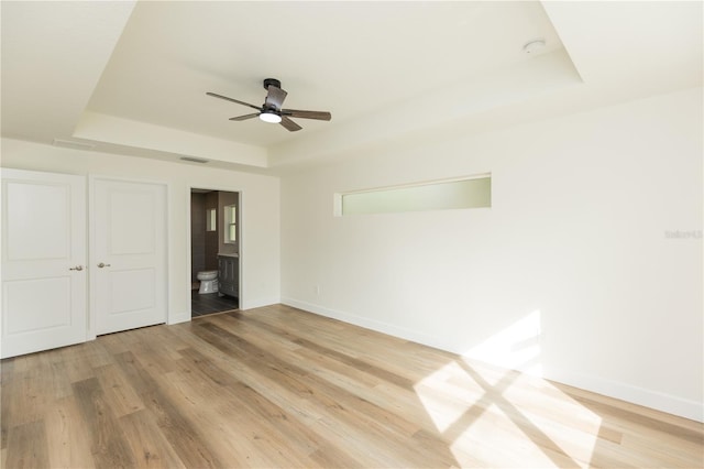 unfurnished bedroom with connected bathroom, hardwood / wood-style flooring, ceiling fan, and a raised ceiling