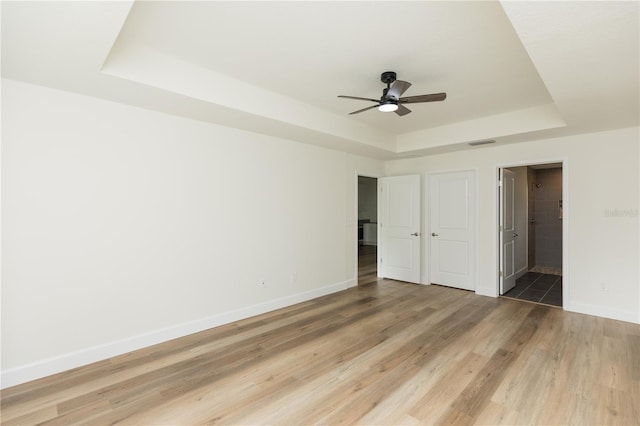 unfurnished bedroom with hardwood / wood-style floors, ensuite bath, ceiling fan, and a raised ceiling