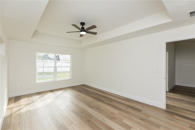 unfurnished room with light hardwood / wood-style floors, ceiling fan, and a tray ceiling