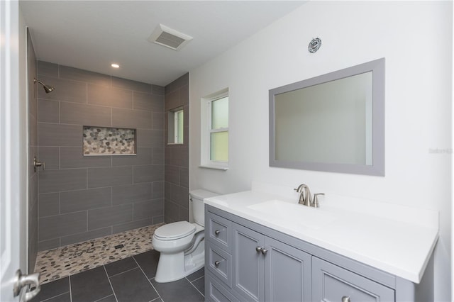 bathroom with toilet, vanity, tile patterned flooring, and tiled shower