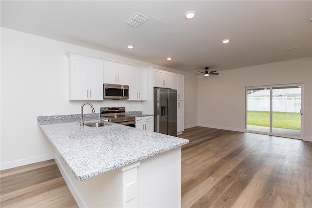 kitchen with sink, kitchen peninsula, appliances with stainless steel finishes, light hardwood / wood-style flooring, and white cabinets