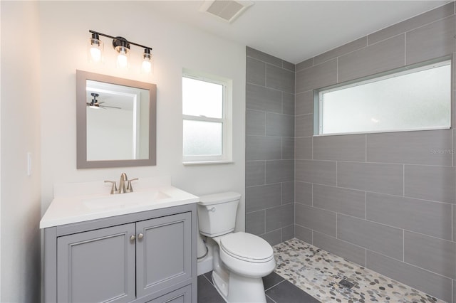 bathroom featuring tiled shower, tile patterned floors, toilet, vanity, and ceiling fan