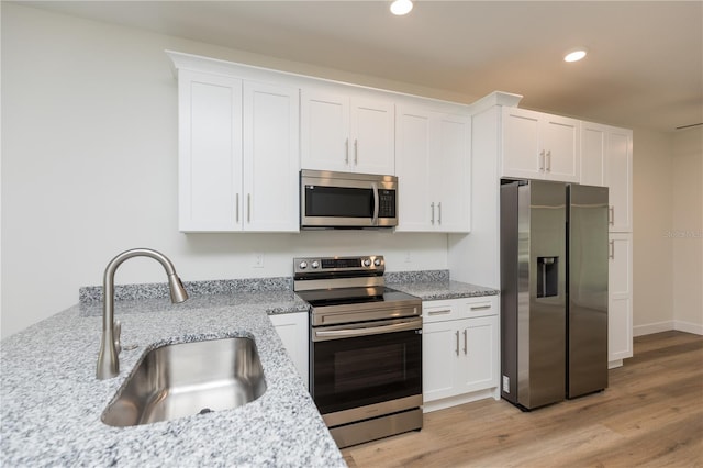 kitchen featuring sink, light stone countertops, white cabinetry, light wood-type flooring, and appliances with stainless steel finishes