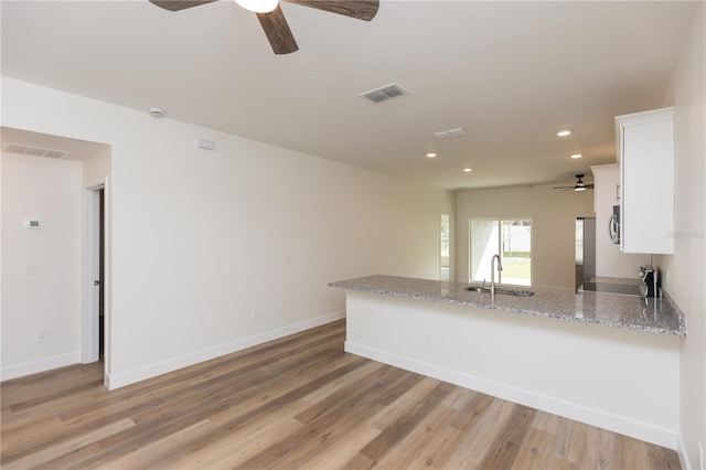 kitchen with white cabinets, light stone countertops, sink, and light wood-type flooring